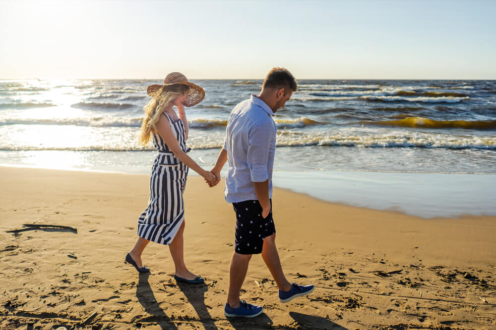 Side view of young couple in love holding hands while walking on sand